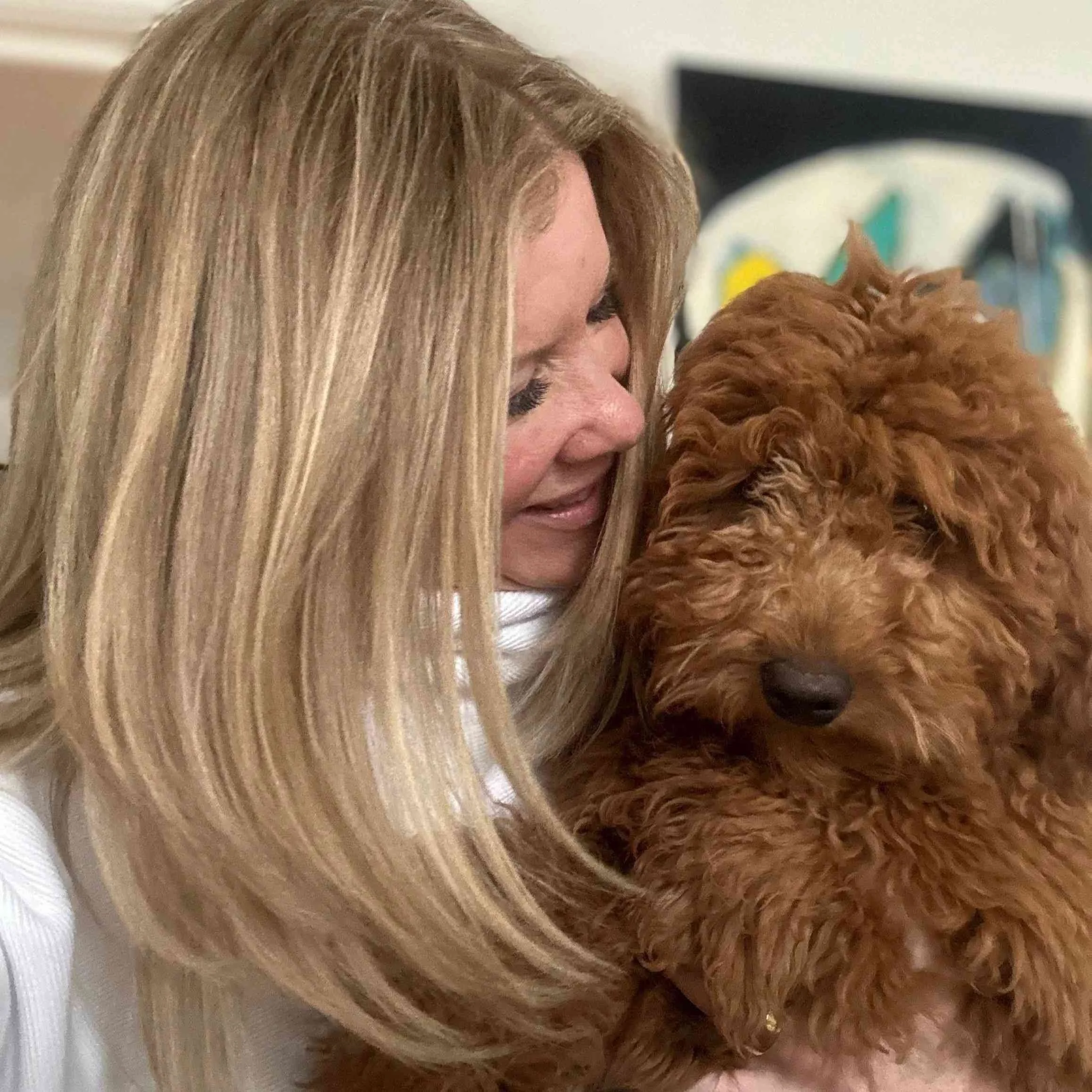 A woman with long blonde hair hugging a brown curly-haired dog, pet psychic near me.
