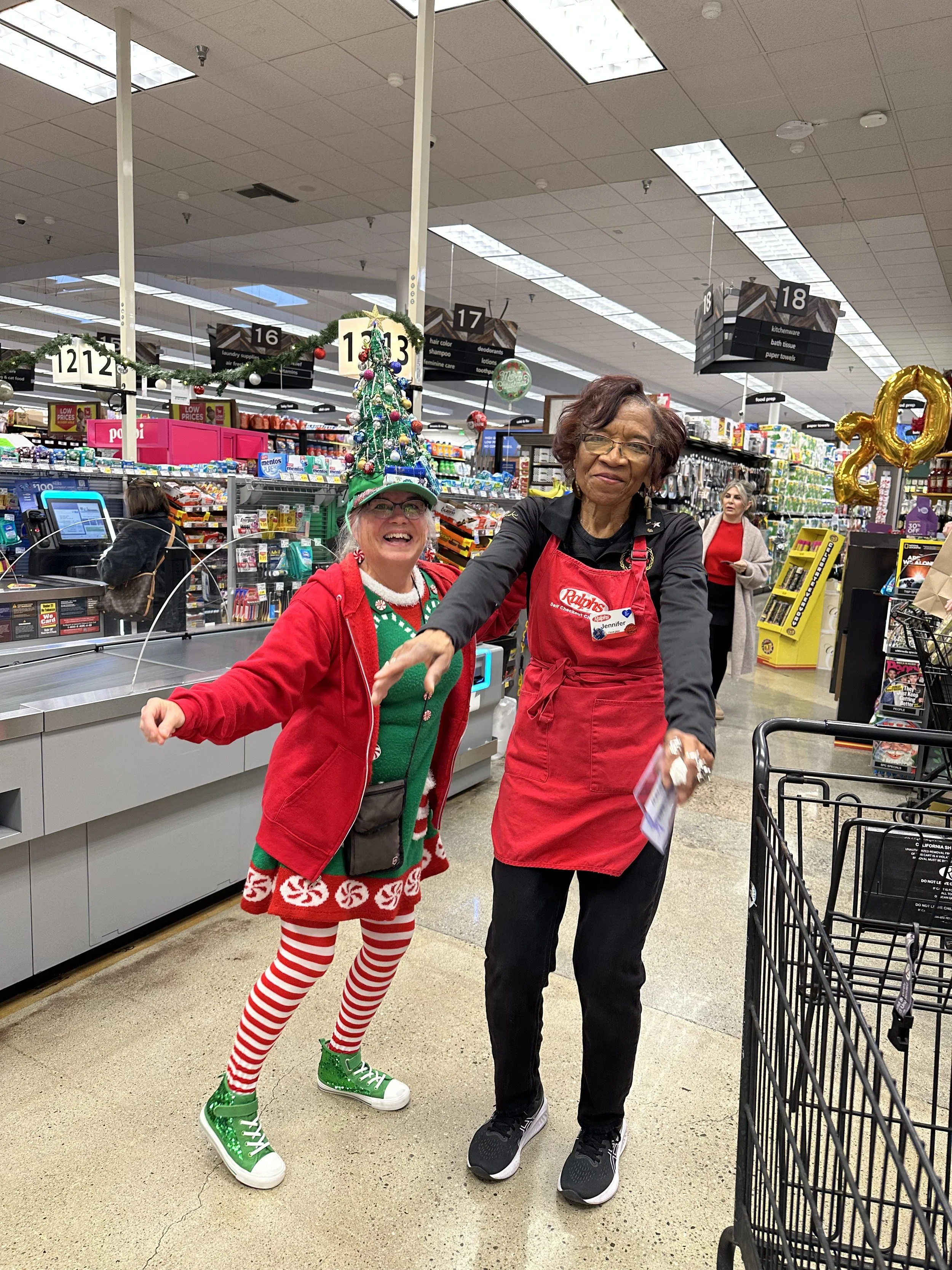 Ms. A in an Elf outfit and a Christmas tree Hat at the local grocery store dancing with an employee