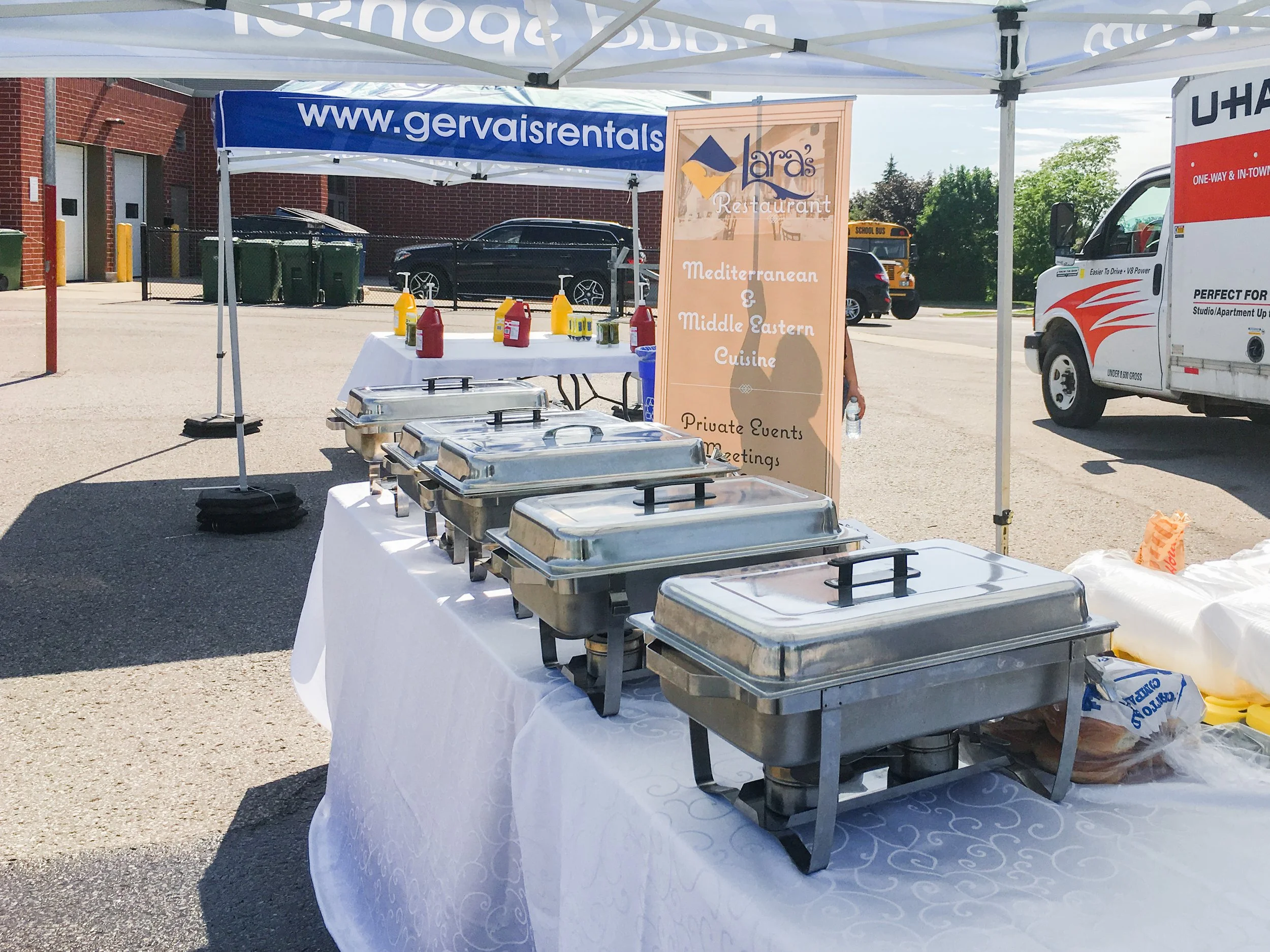 Buffet table with chafing dishes, condiments, and a sign for Lara's Mediterranean and Middle Eastern Cuisine at an outdoor event.