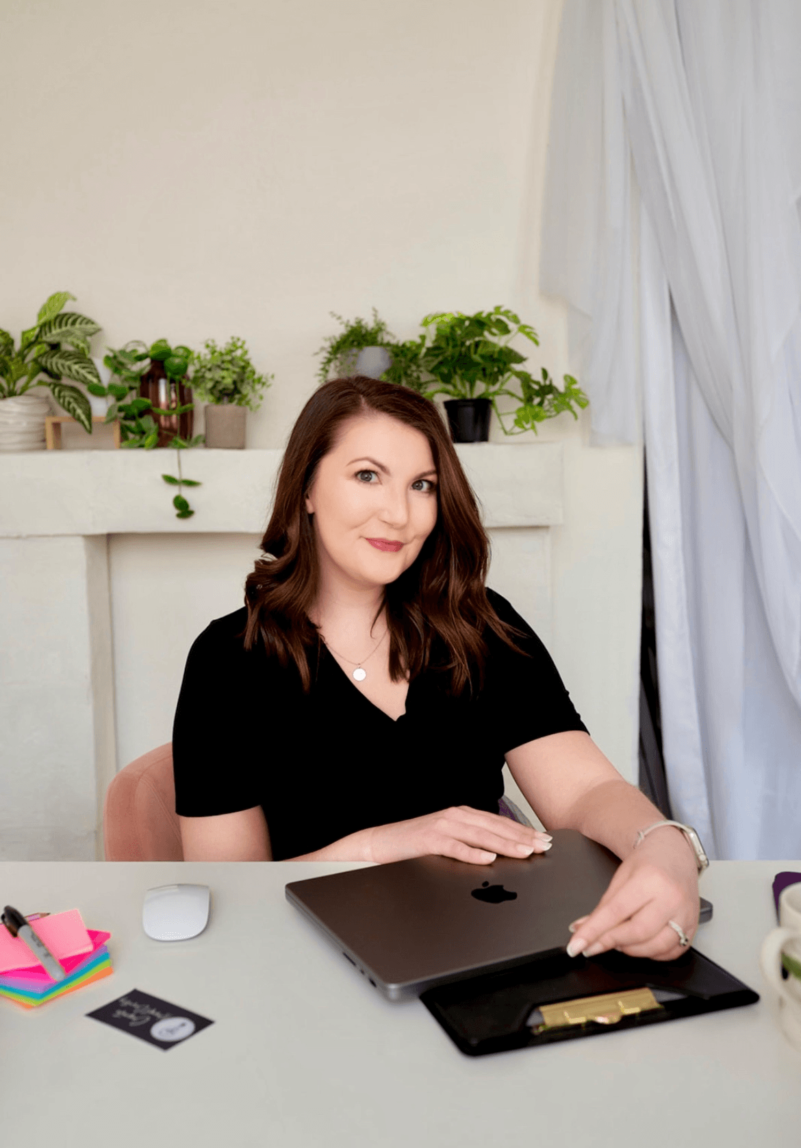 A woman with shoulder-length brown hair wearing a black shirt, sitting at a desk