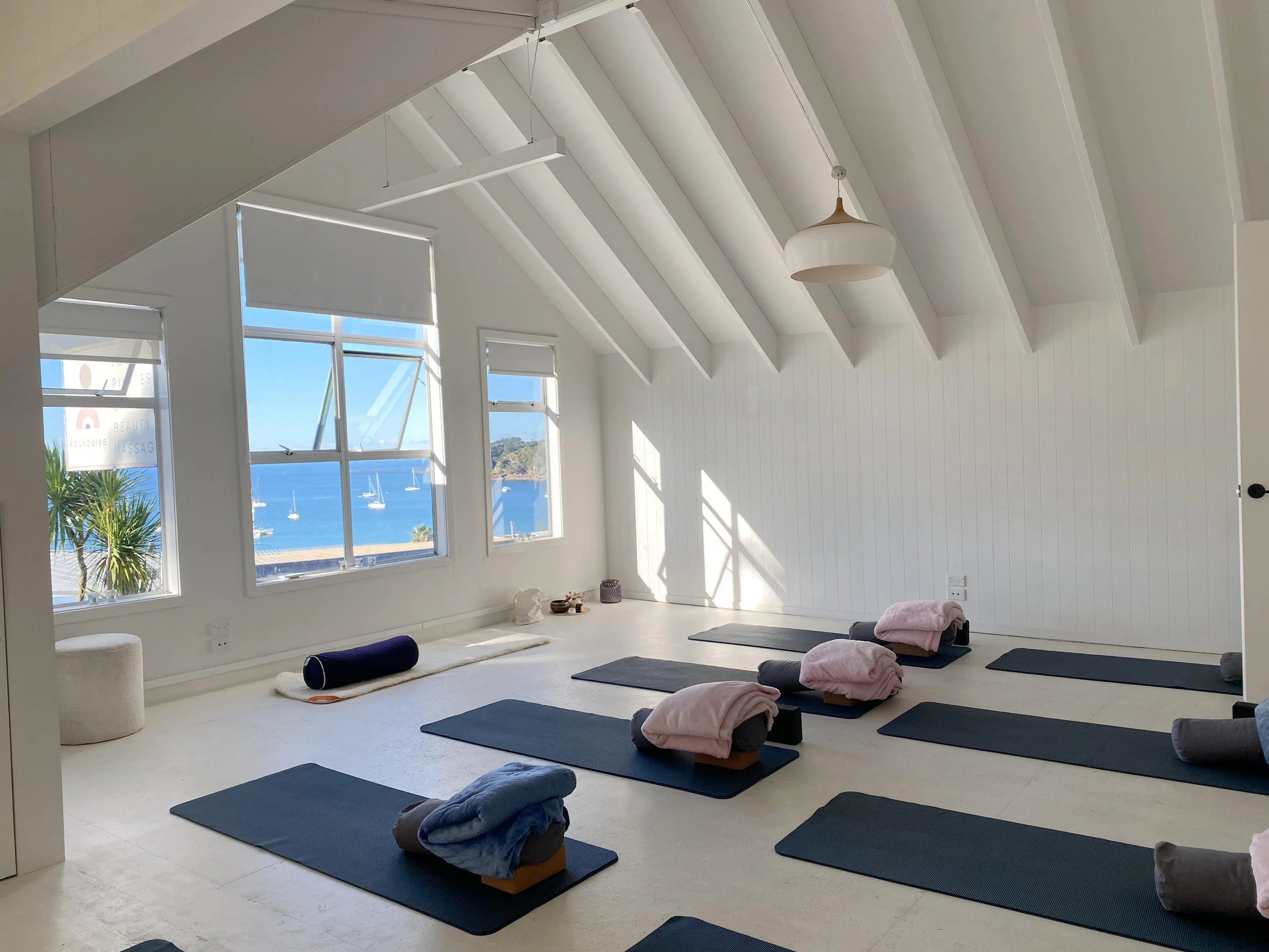 Yoga studio with black mats, rolled-up towels, and a view of the ocean through large windows.