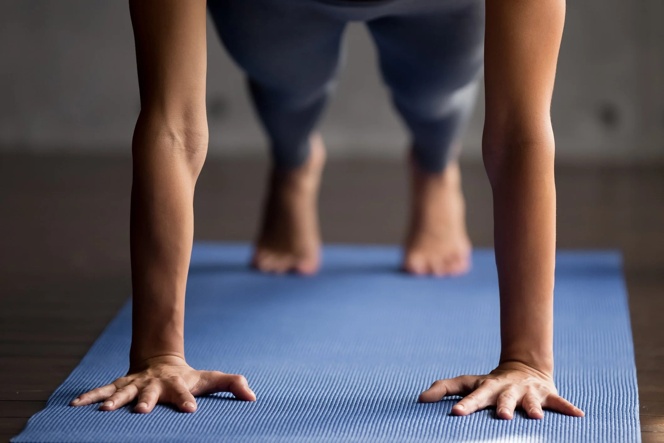 Close-up of a person doing a plank exercise on a blue yoga mat, with a focus on the arms and hands.