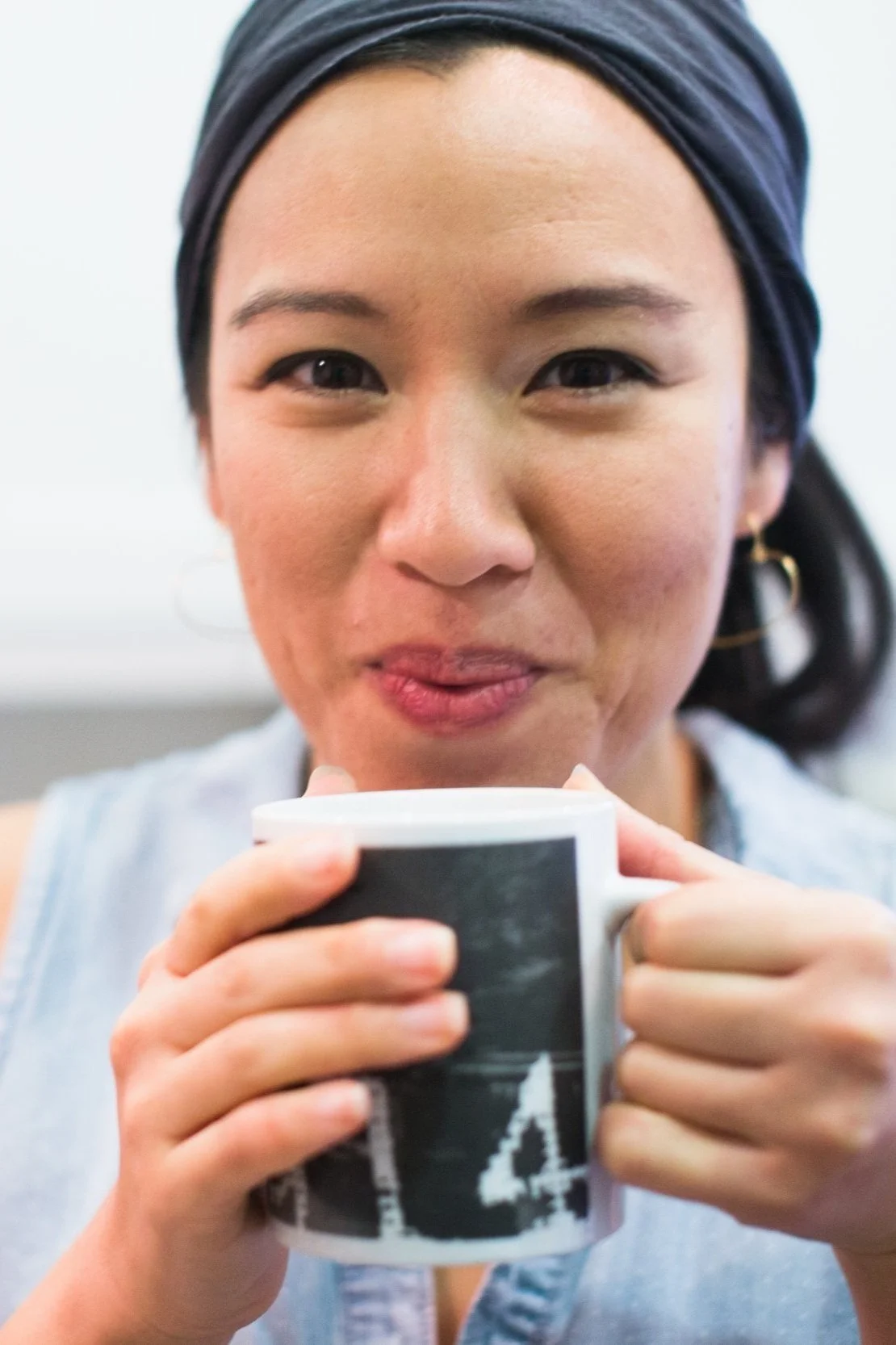 Woman with dark hair wearing a headscarf, holding a coffee mug and smiling.