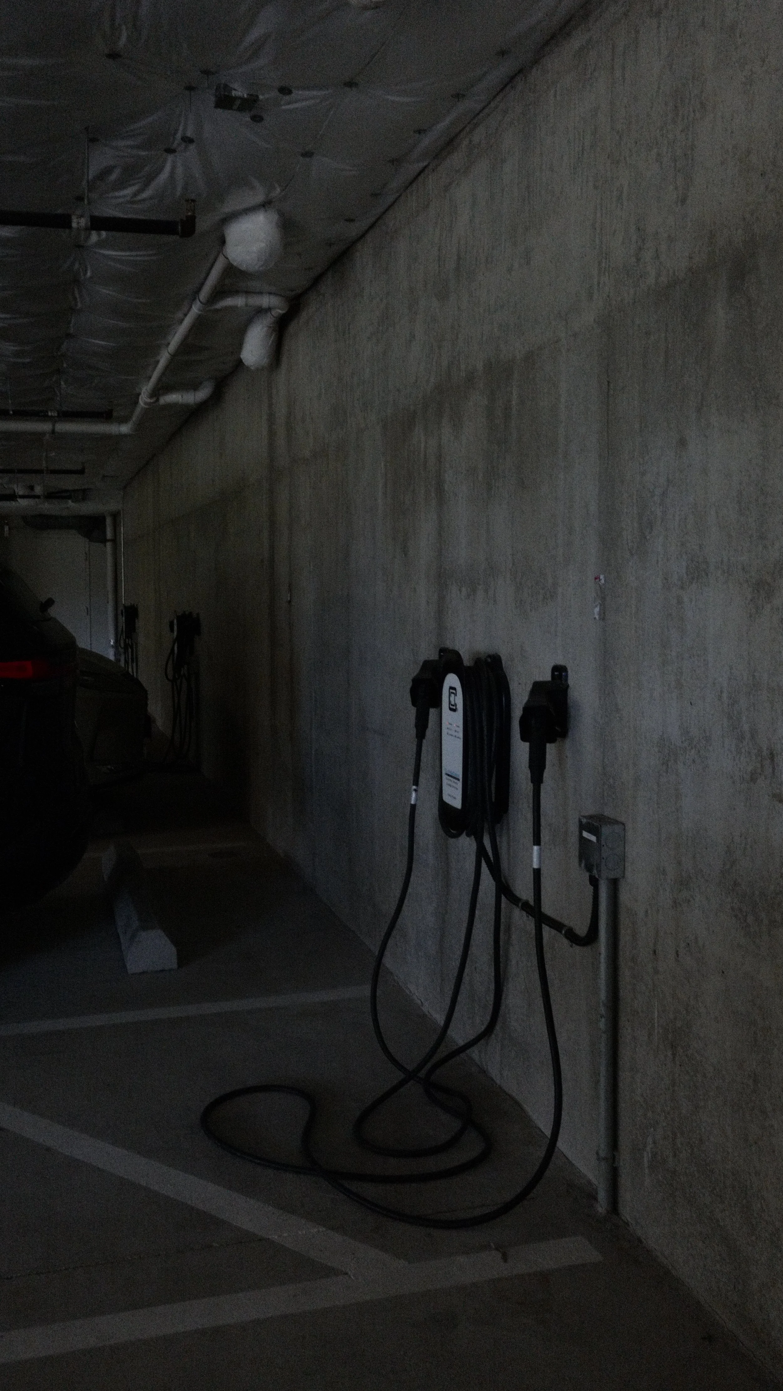 Electric vehicle charging station with two charging cables mounted on a concrete wall in a parking garage.