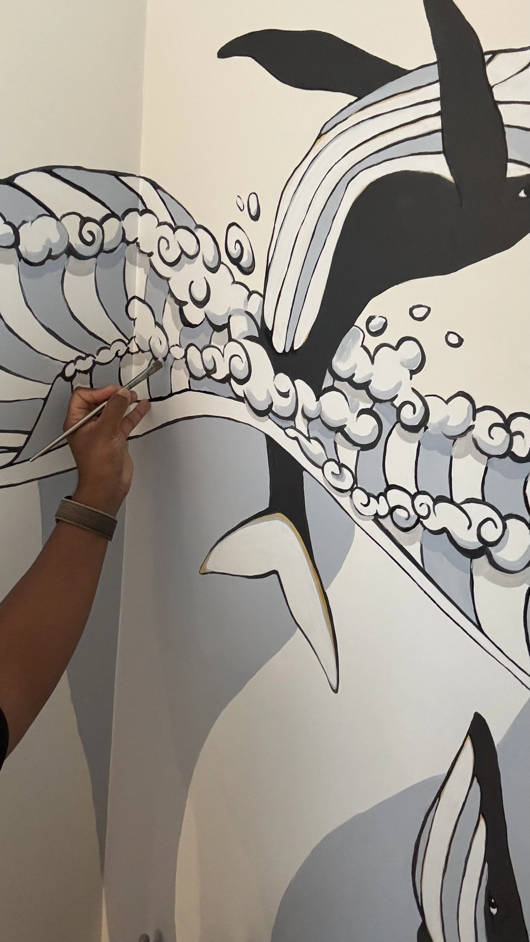 A person is painting a large black and white mural of a whale jumping out of the water with waves and bubbles.