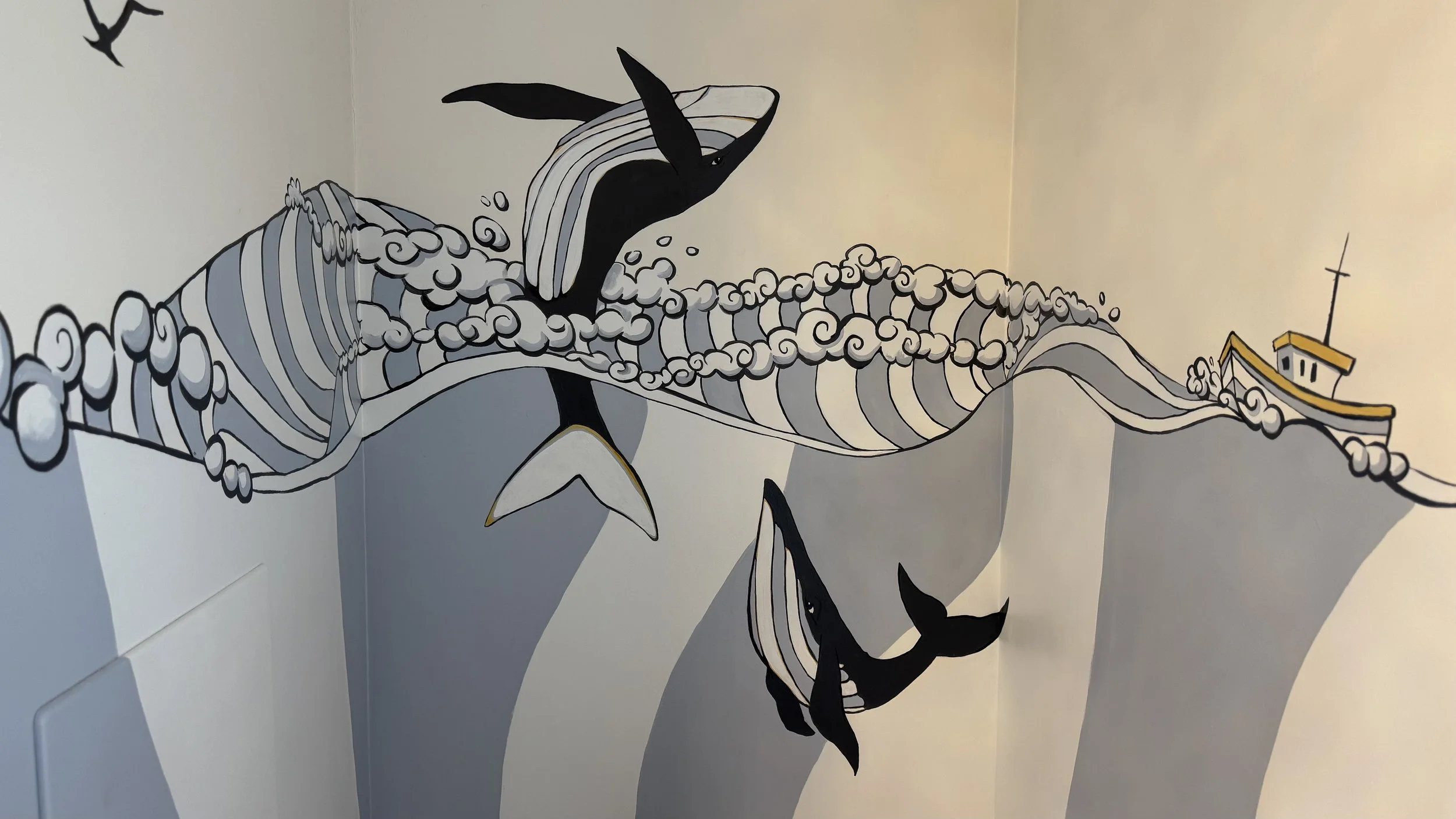 A mural of a whale jumping out of stylized ocean waves, with a small boat on the horizon, painted on a corner wall.