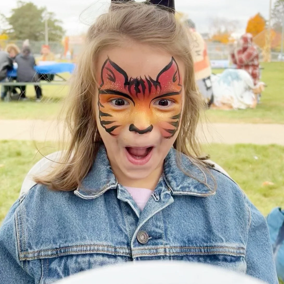 Girl with her face painted looking into the mirror at her face painting. She is so surprised by her face paint!