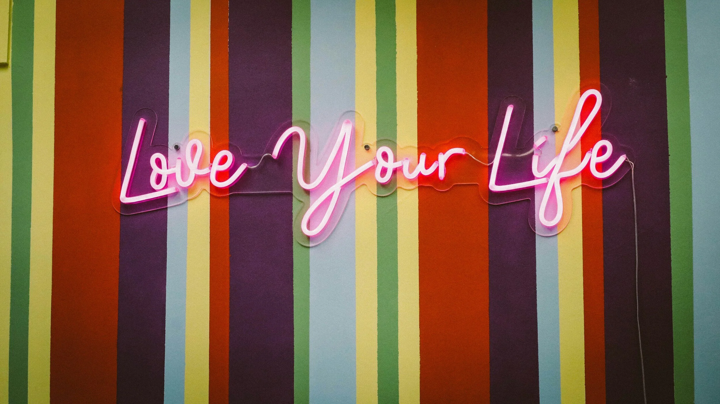 "Love Your Life" neon sign on a colorful striped wall.