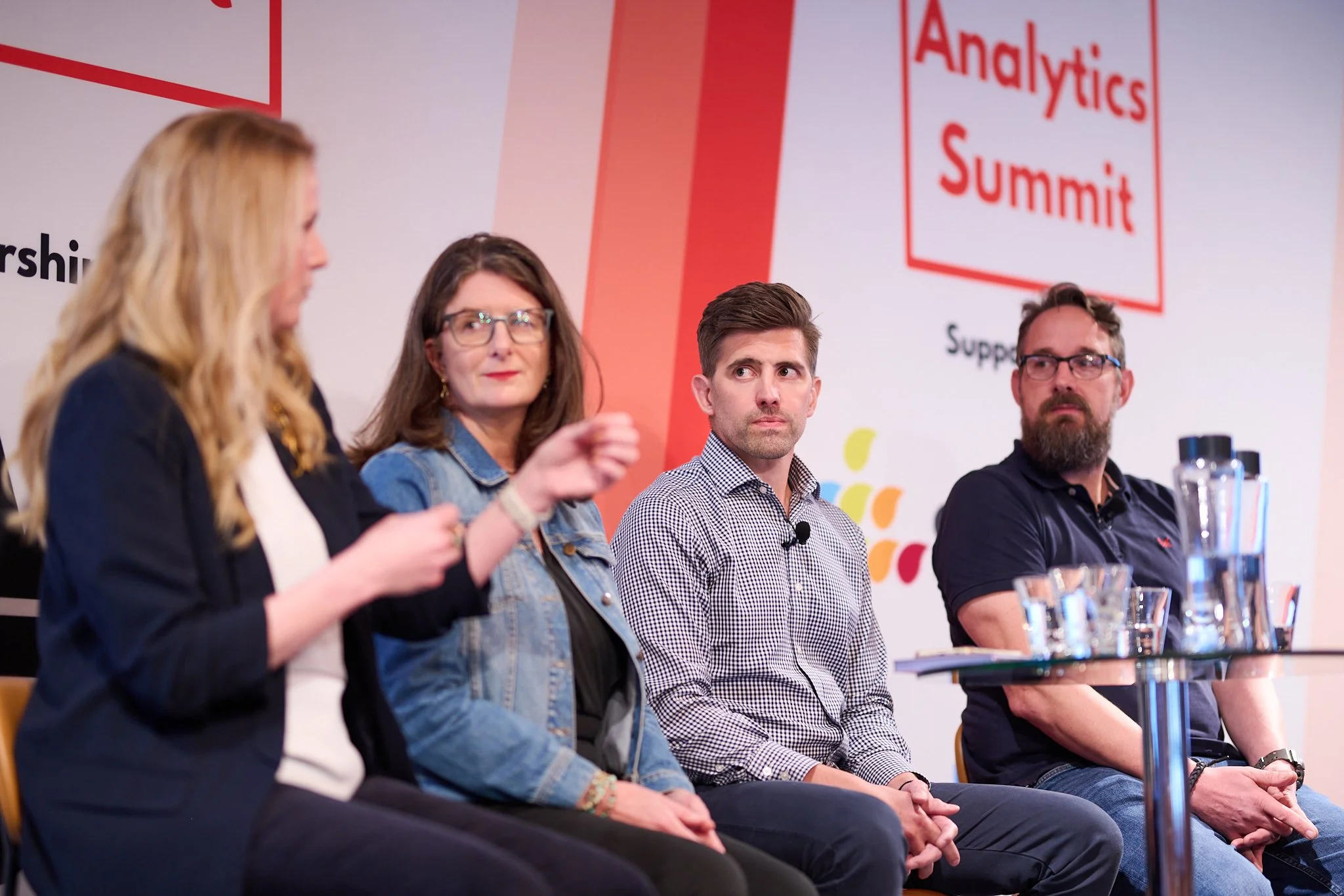 Four people on a panel discussion at an Analytics Summit, with microphones and a table in front.