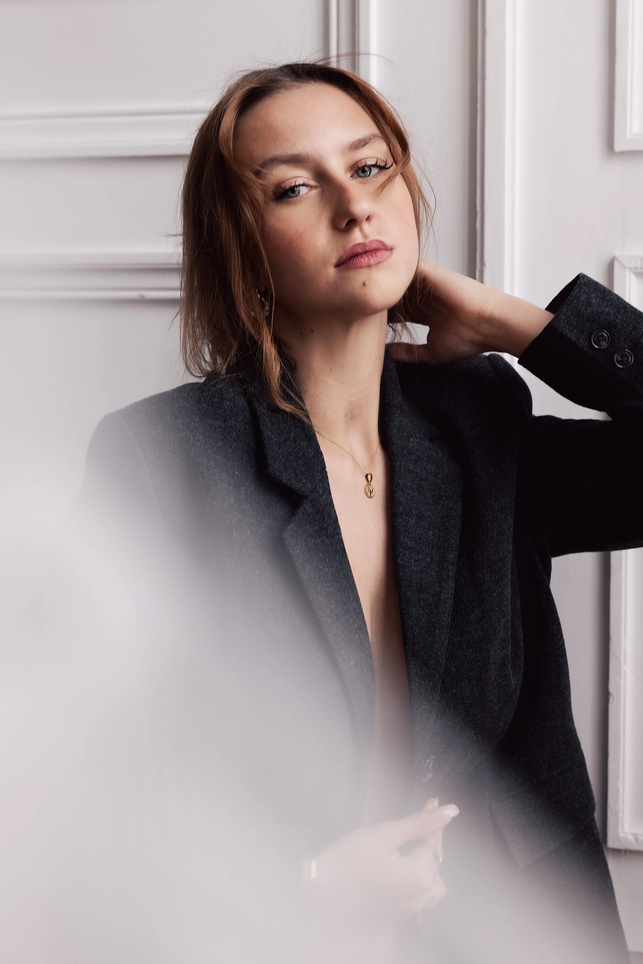Jeune femme avec cheveux bruns et chemise noire, posant contre un mur blanc
