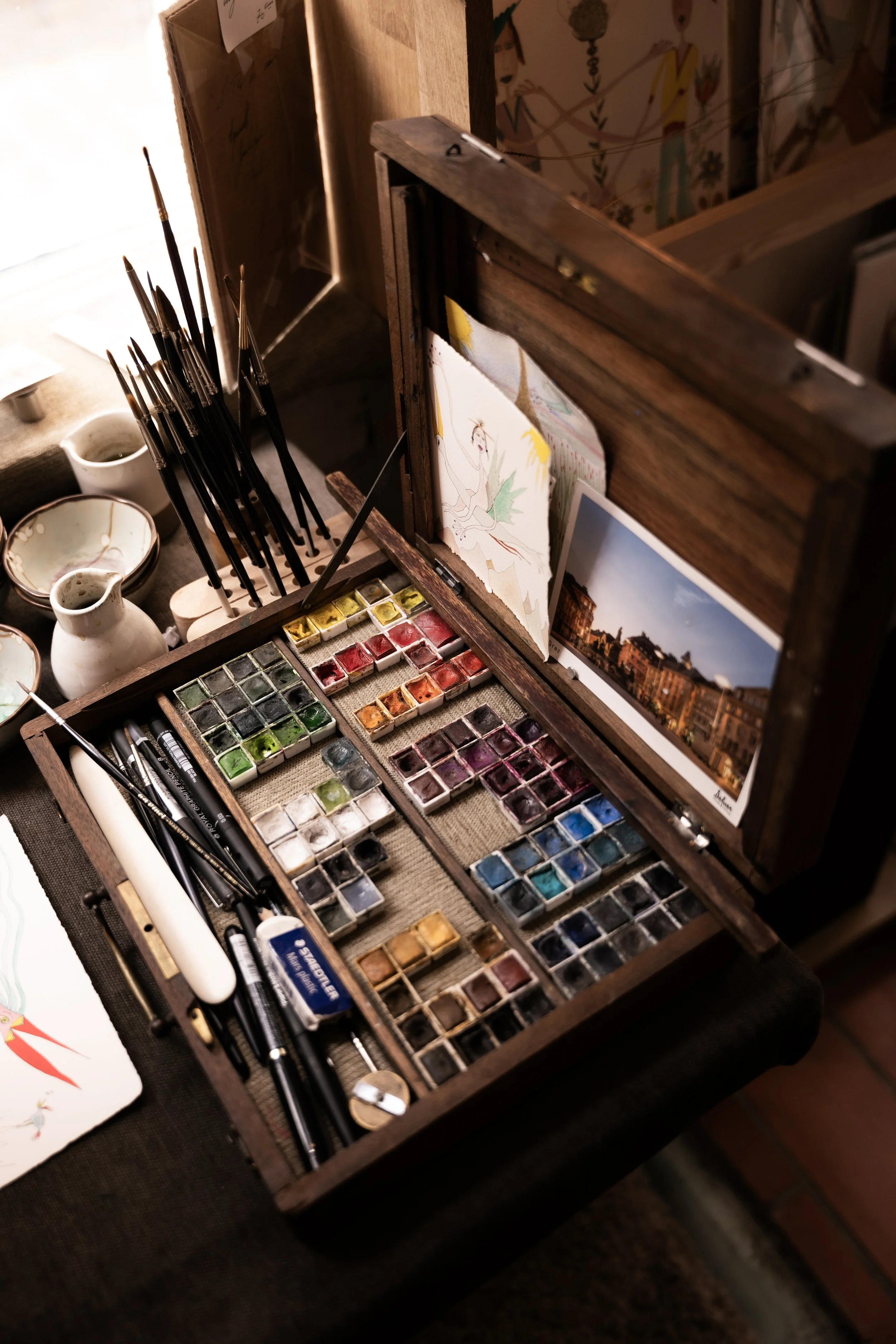 Une boîte à peinture avec des aquarelles, des pinceaux, des pots de peinture, et des illustrations artistiques à l'intérieur.