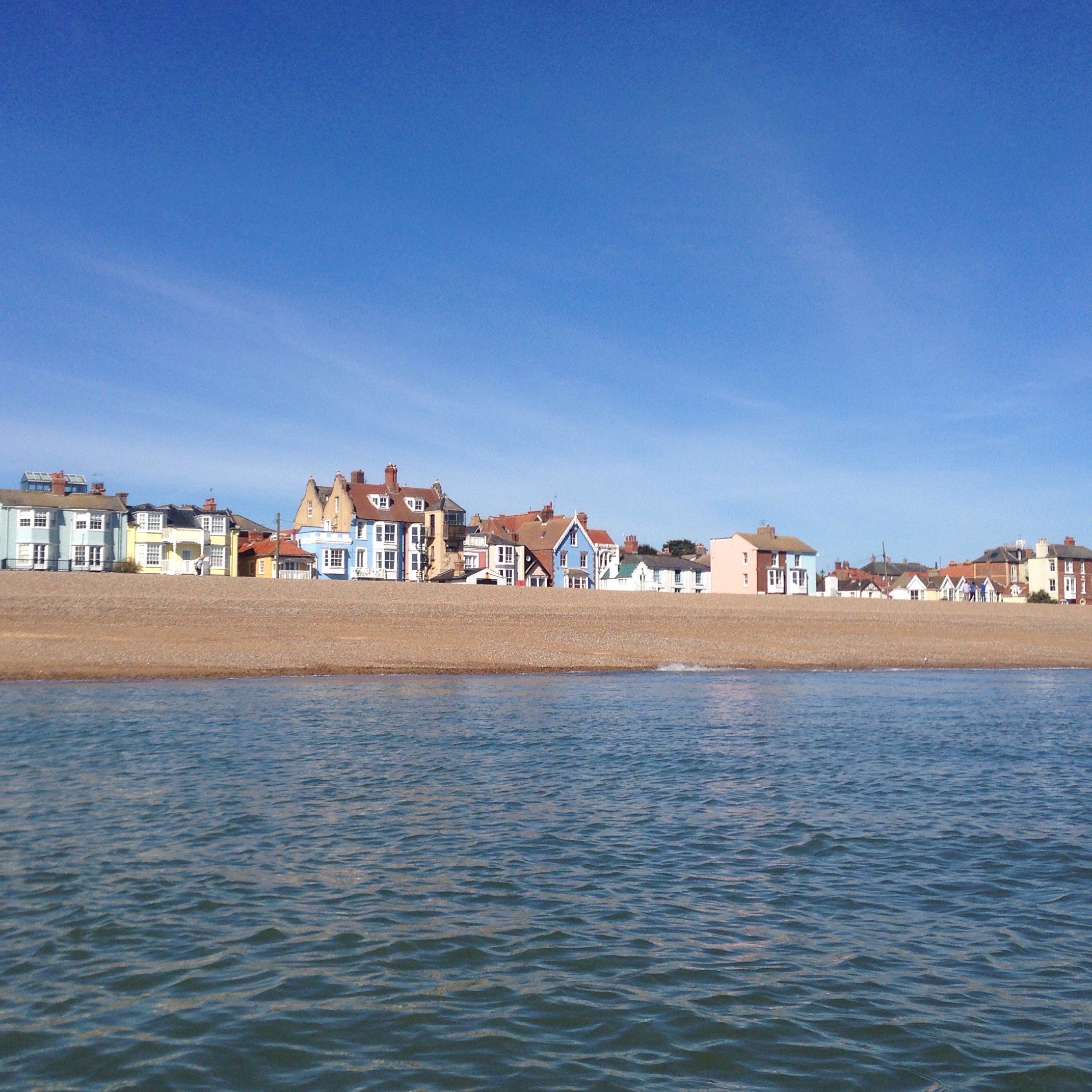 Row of colourful houses along a pebble beach with blue sky and sea in the foreground.