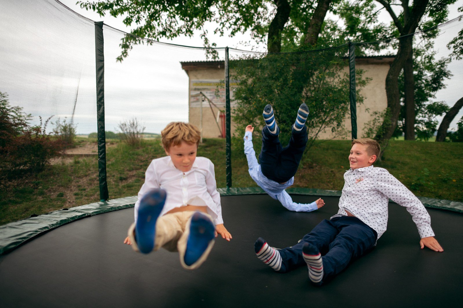 Tři děti skáčou na venkovní trampolíně.