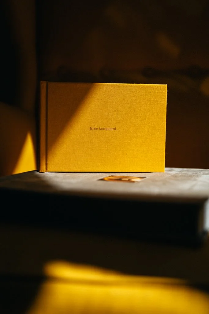 A yellow book with the text "Jsme kompletní..." on a table, partially lit by sunlight.