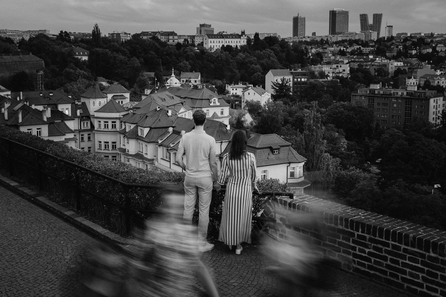 Černobílý široký záběr páru na vyhlídce nad městem.