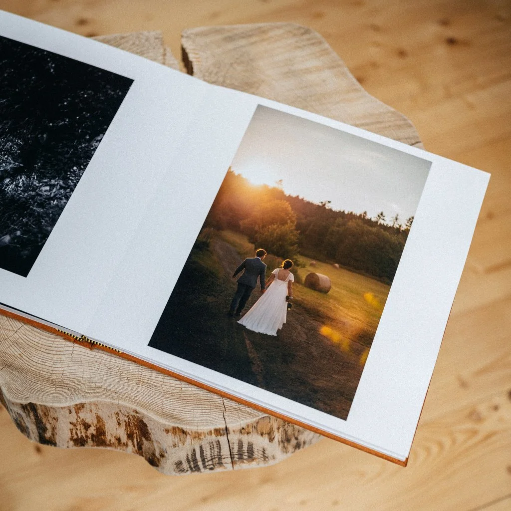 Open photo album with a wedding photograph, showing a bride and groom holding hands and walking through a field at sunset.