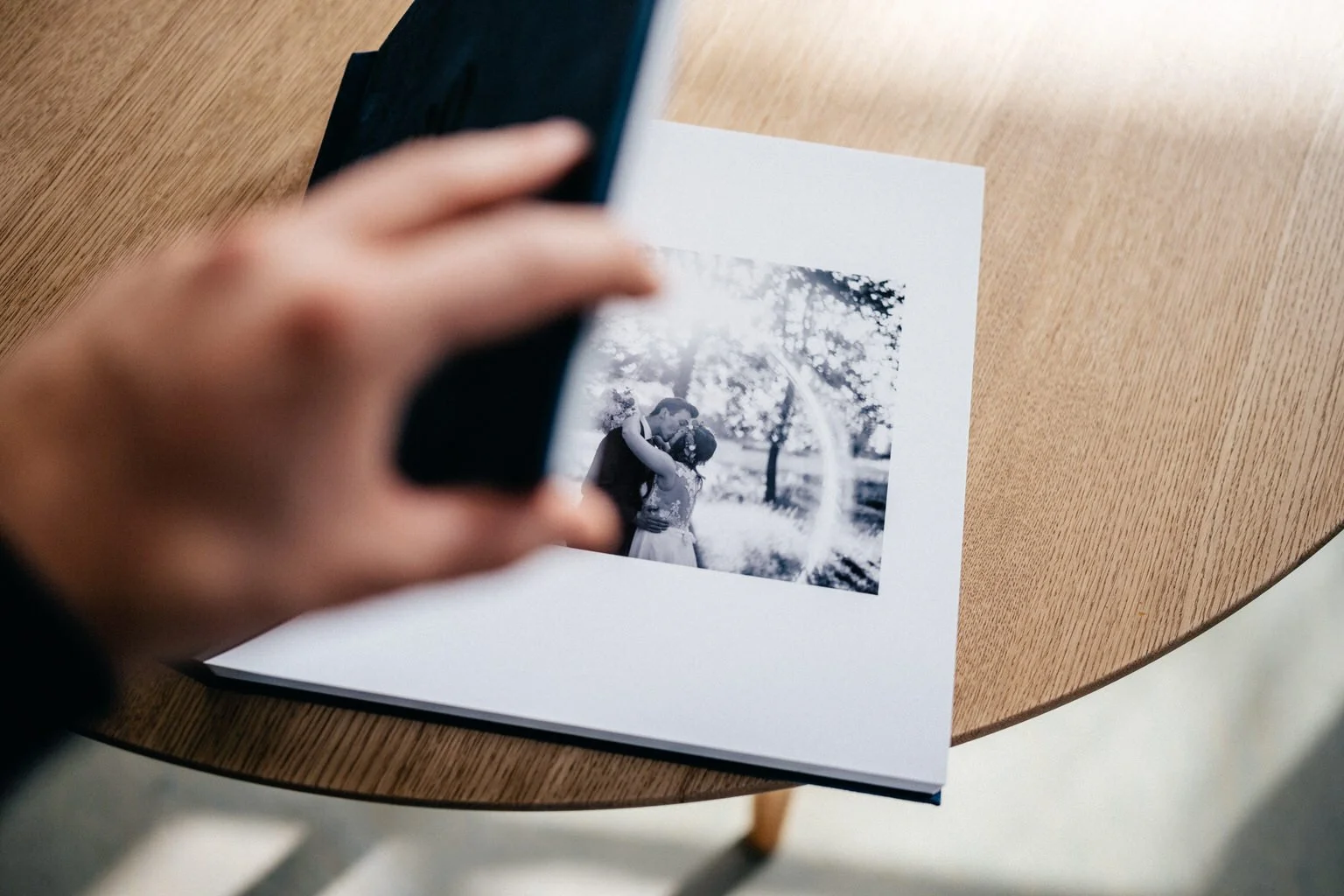 Person holding photo album page with black and white photo of couple kissing in outdoor setting.