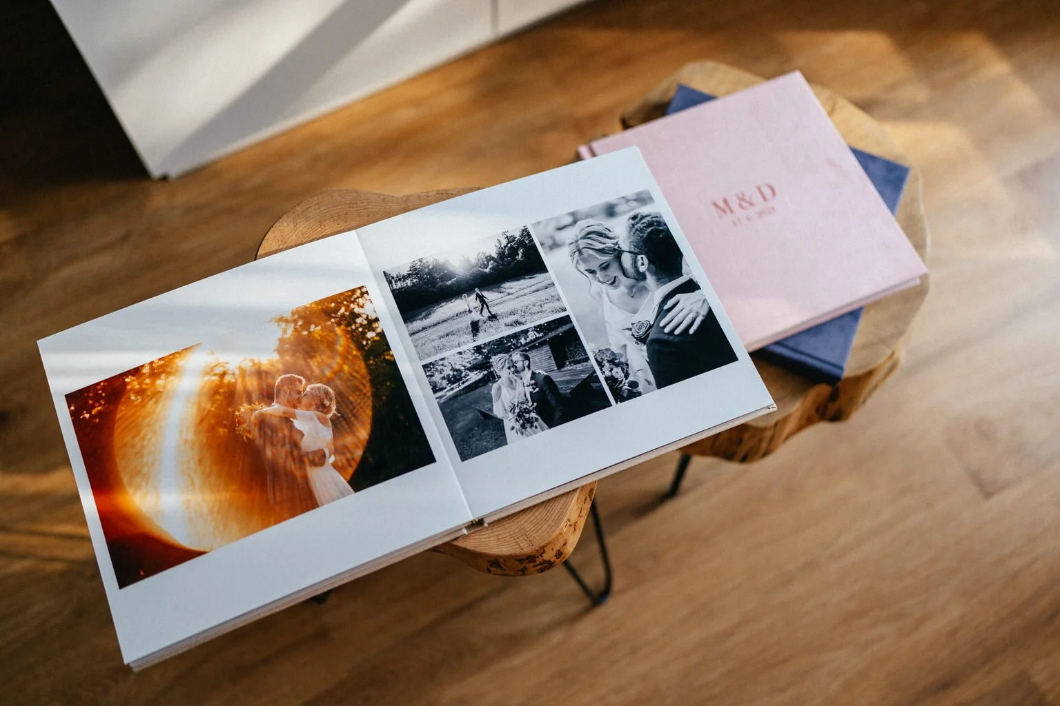 Open wedding photo album on a wooden table showing several wedding photographs, with additional closed albums nearby.