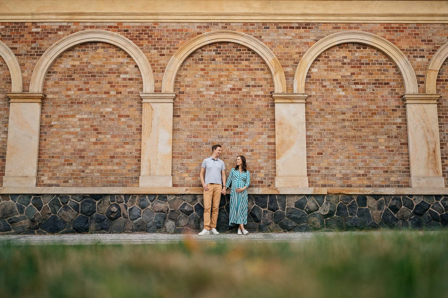 Andrea a Filip stojí pod prostředním obloukem vysoké cihlové zdi.