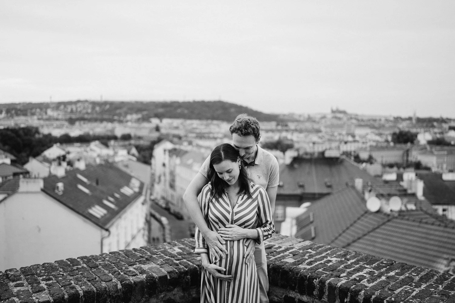 Černobílý portrét Andrey a Filipa u vyhlídky s pražskými střechami v pozadí.