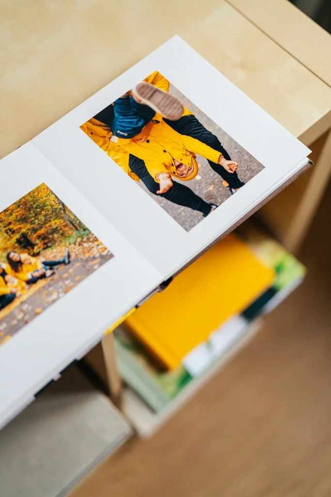 Open photo album on a table showing a child in a yellow coat and beanie, playful pose outdoors.