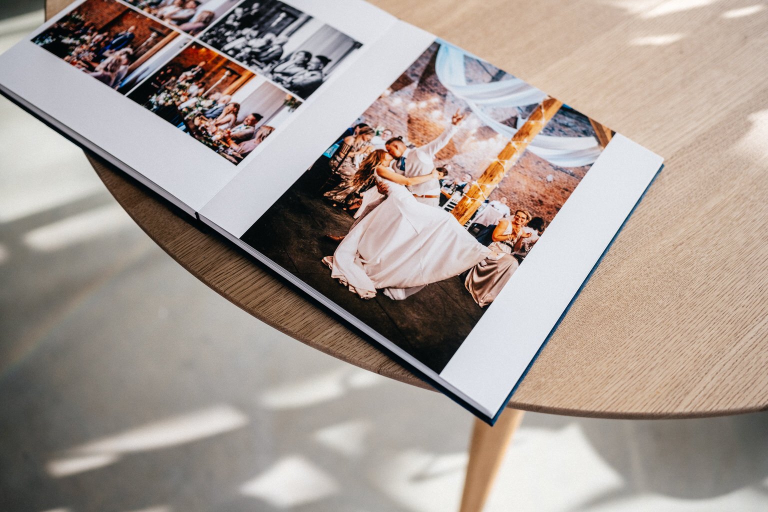 Open wedding photo album on a wooden table, showing a bride and groom dancing and other wedding scenes.