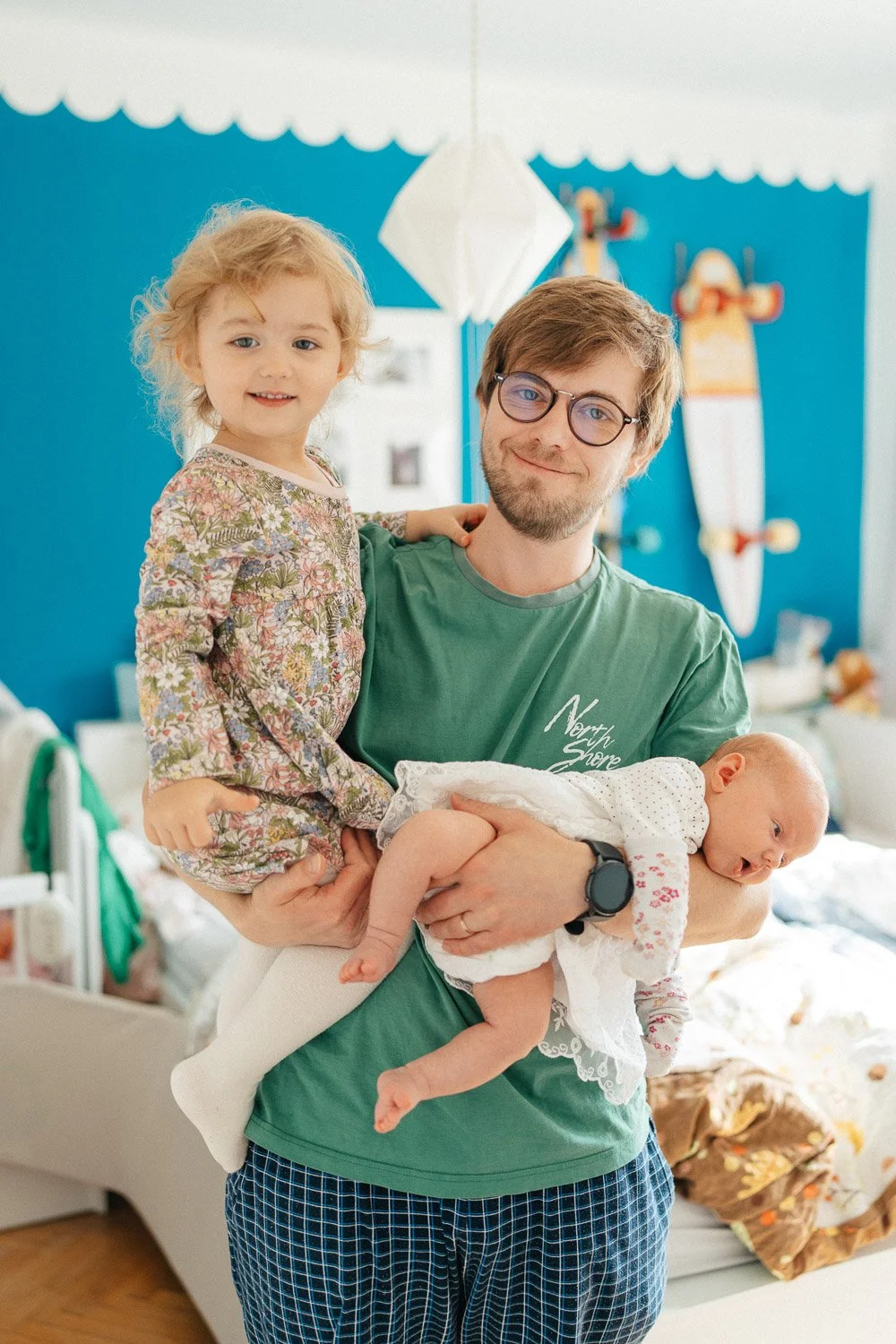Muž v zeleném tričku drží v náručí malou dívku i miminko.