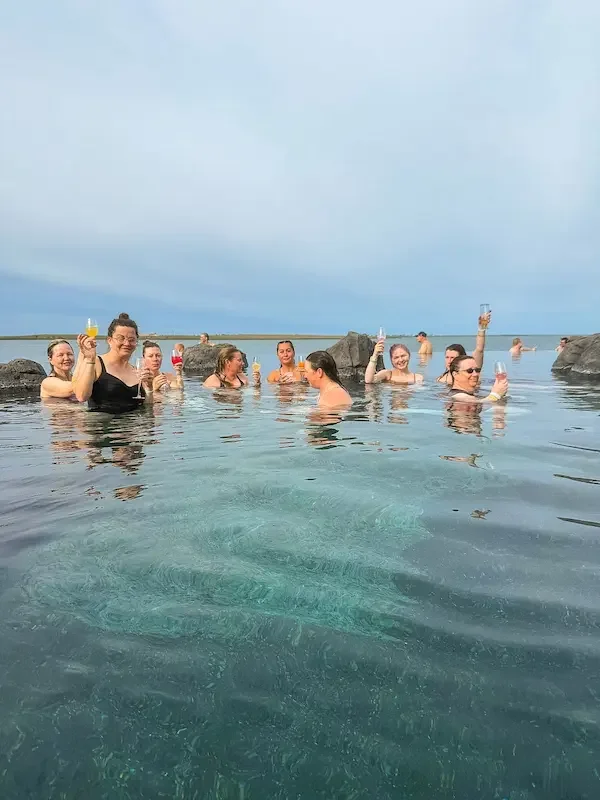 group of women enjoying a hot spring with ocean in background in iceland