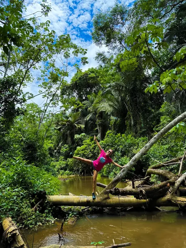 woman balancing on log crossing stream in amazon rainforest