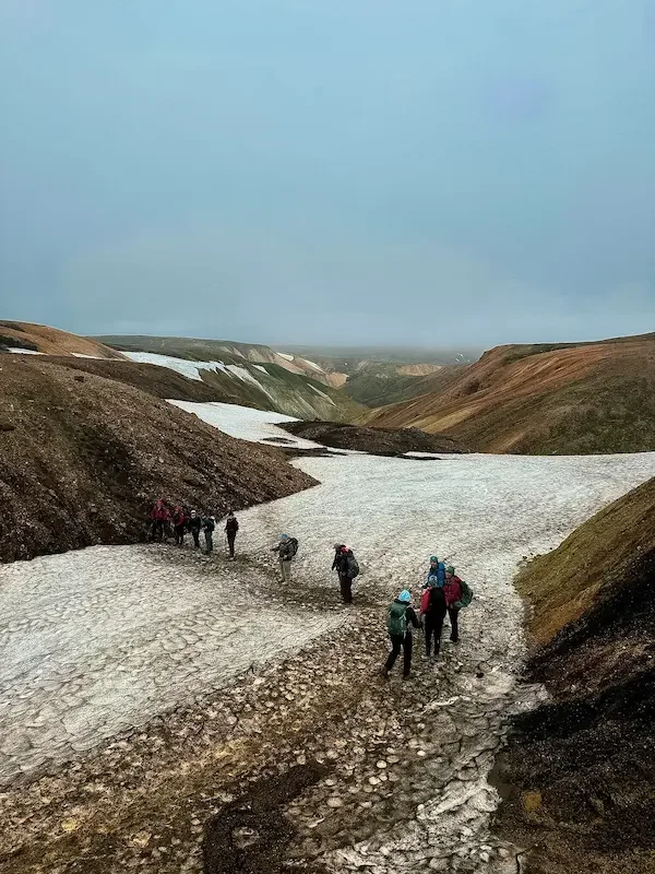 hikers on laugavegur trek crossing snowy glacier patch in iceland
