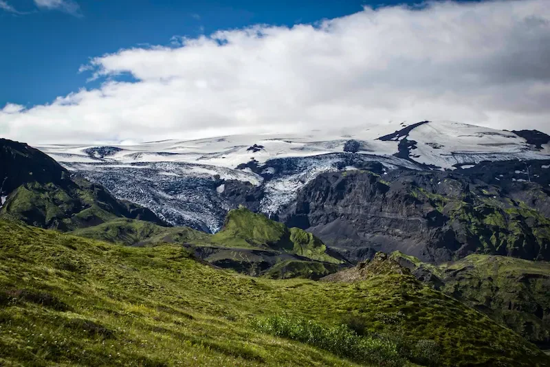 snowy mountain in distance wtih green hills in front in iceland