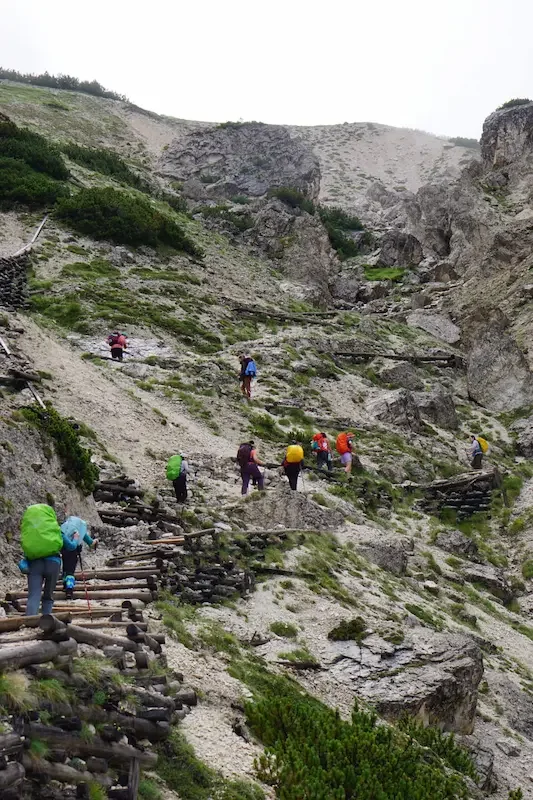 backpackers hiking up rocky stair trail in dolomites