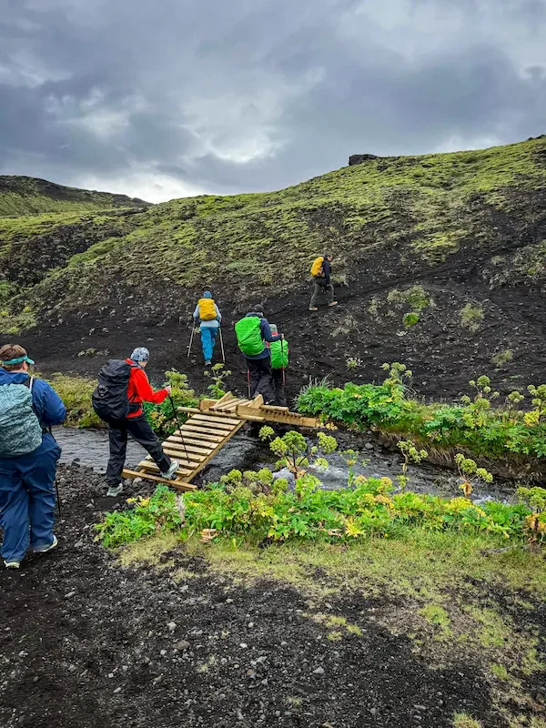 hikers crossing a small stream on a little bridge on laugavegur trek in iceland
