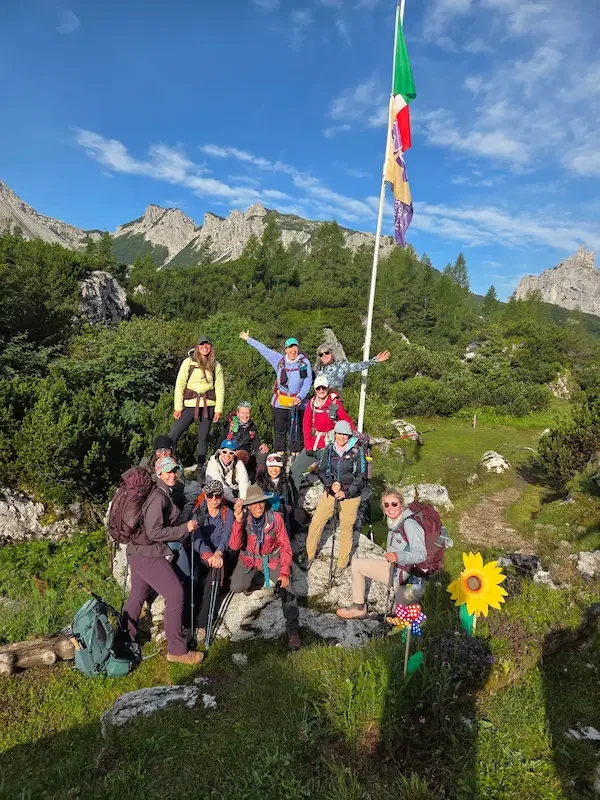group of hikers in front of italian flag and dolomites mountains and trees behind