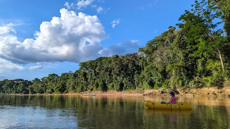 yellow inflatable kayak on amazon river surrounded by jungle and blue sky