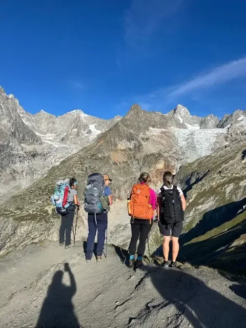 four hikers on rocky tour du mont blanc trail viewing the alps 