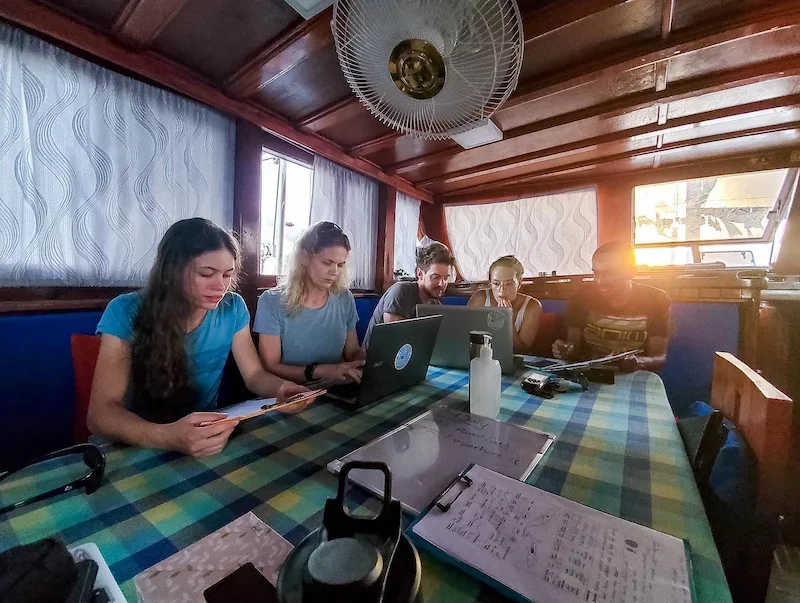 group of researchers on computers aboard a sailboat