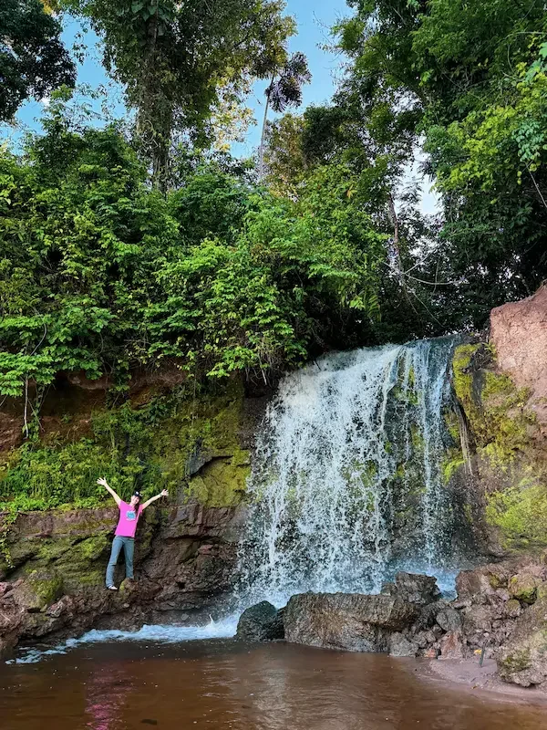 woman with arms up posing in front of waterfall flowing into amazon river