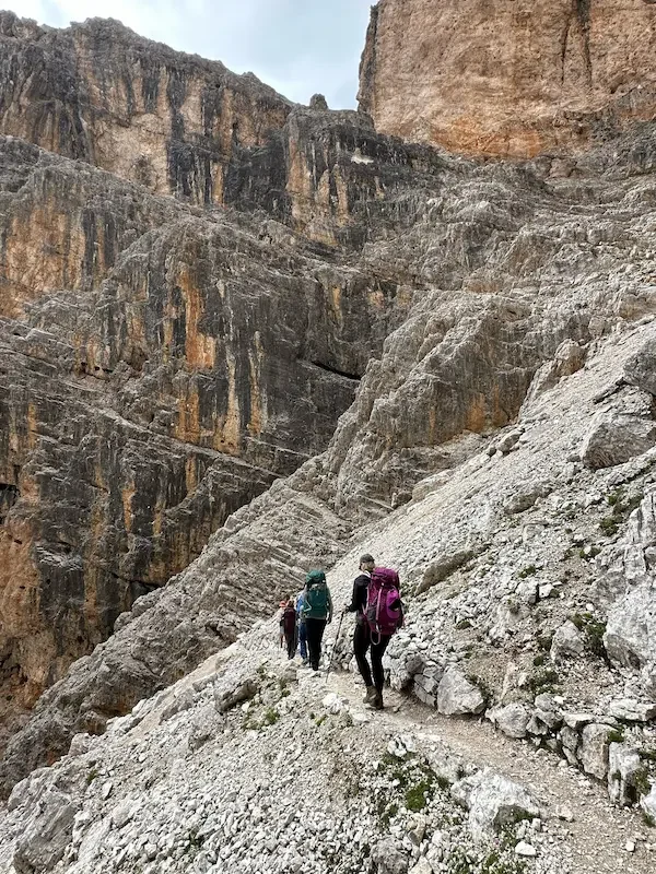 hikers on rocky trail with steep edge in dolomites itals