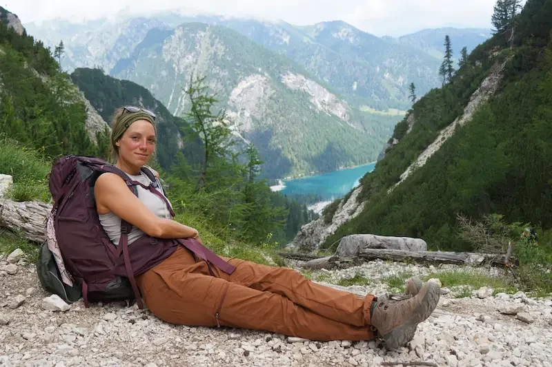 woman hiker wearing backpack and sitting on ground overlooking lake in dolomites mountains