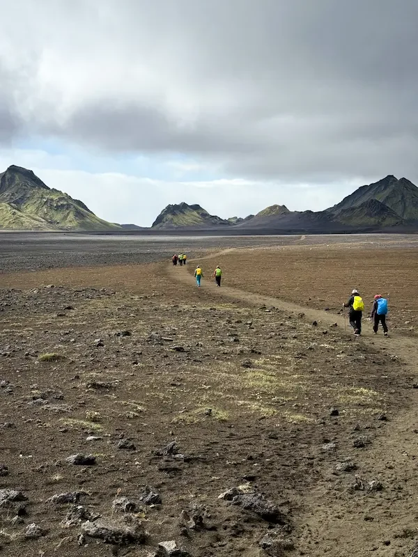 hikers on flat volcanic part of laugavegur trek in iceland and mountains in distance