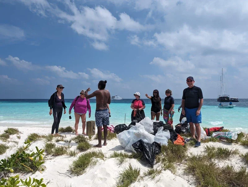 group of people gathered on white sand beach to pick up trash