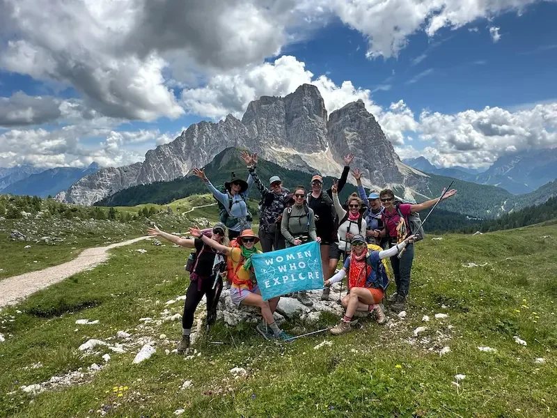 group of hikers holding flag in dolomites with blue skies
