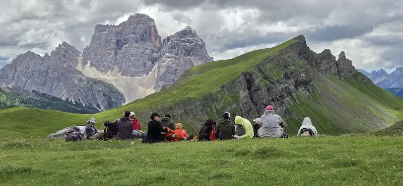 hikers resting on green grass with dolomites in background