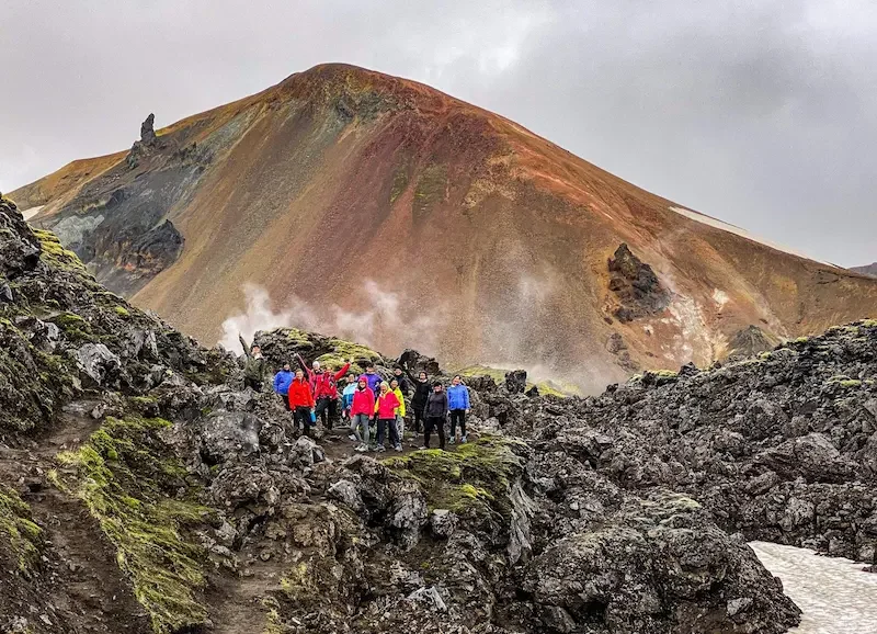 group of hikers in bright jackets standing in front of volcanic mountain in iceland