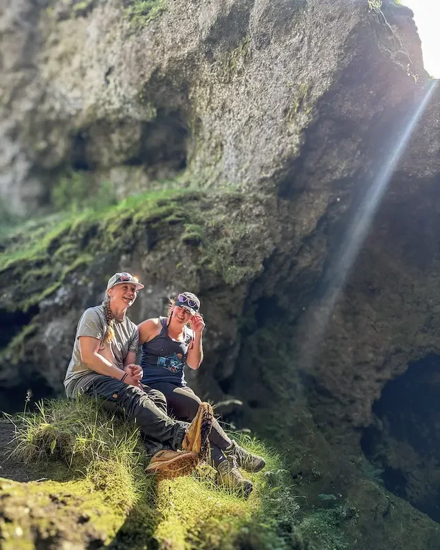 two friends sitting on grassy overlook in iceland