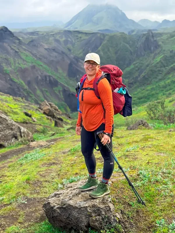 hiker in orange shirt standing on rock over green valley in iceland
