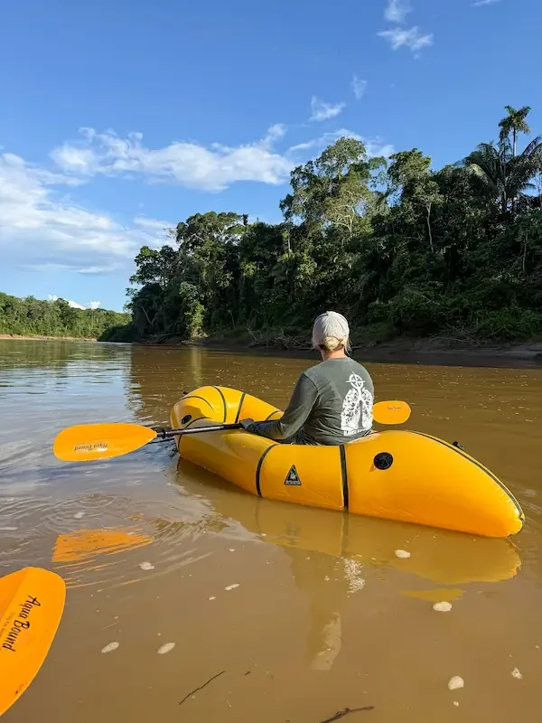 person in yellow kayak floating down amazon rainforest looking at jungle on shoreline