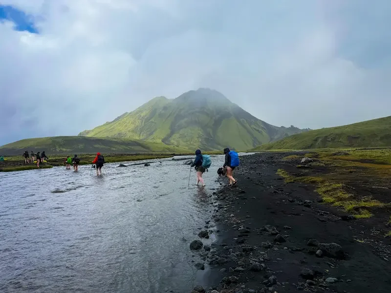 hikers crossing river on laugavegur trek in iceland