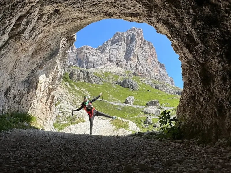 hiker doing starfish pose through a cave entrance with dolomite mountains